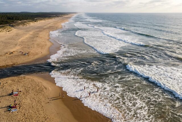 Vue aérienne d'une plage landaise : une bande d'eau sombre part du rivage vers le large en coupant la ligne d'écume, les vagues déferlant de part et d'autre sur les bancs de sable
