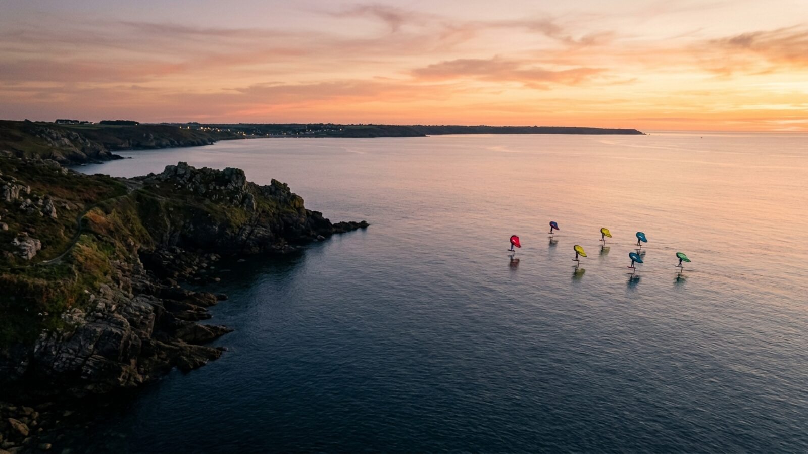 Plusieurs wingfoilers naviguant dans une baie profonde au crépuscule