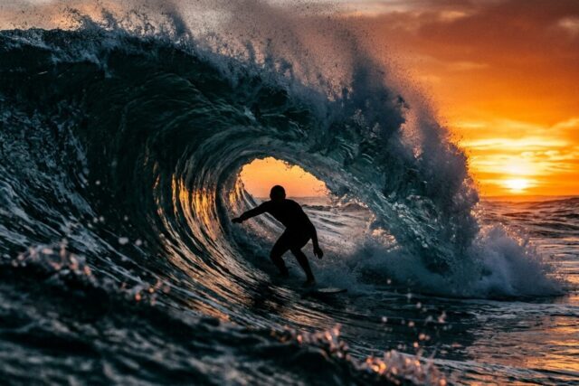 Un surfeur en silhouette à contre-jour dans le tube d'une grosse vague creuse, la lèvre se refermant au-dessus de lui au coucher du soleil