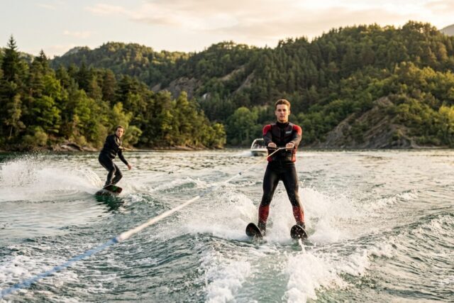 Un skieur nautique de face sur deux skis au premier plan et un wakeboardeur de profil sur sa planche en arrière-plan, tous deux tractés, gerbes d'eau